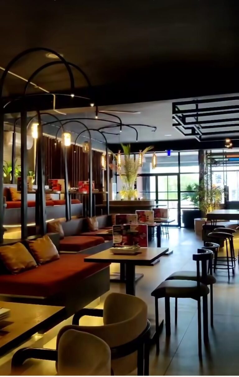 A street-facing cafe interior with arched glazing, pendant lighting, and casual seating, designed by ZM Architects.