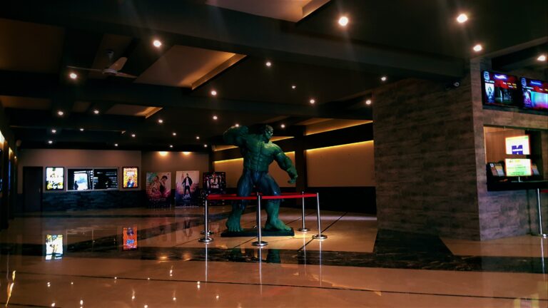 A themed cinema lobby with dark marble flooring, a feature statue, and film-poster display walls, designed by ZM Architects for an entertainment venue.