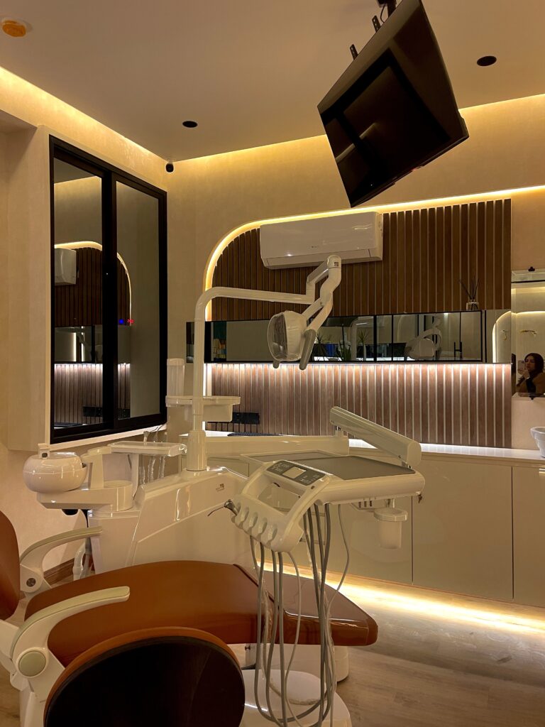A dental clinic interior with warm wood paneling, backlit mirror walls, and integrated dental equipment, designed by ZM Architects for a healthcare client.
