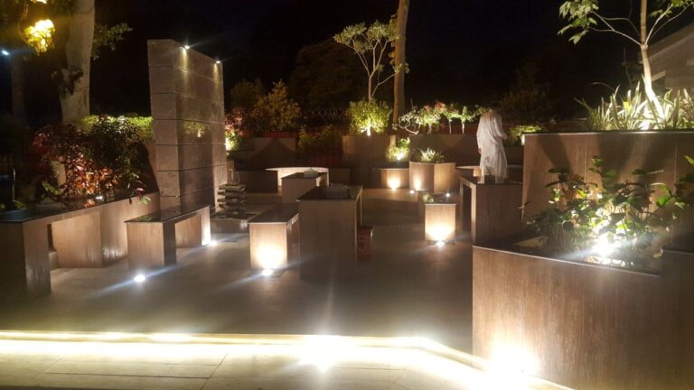Sculptural concrete seating and planters illuminated with warm accent lighting, part of an outdoor hospitality landscape by ZM Architects.