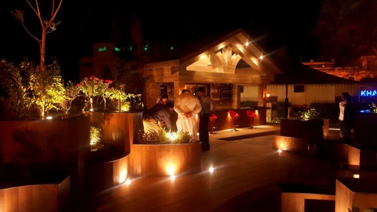 An outdoor restaurant lounge with warm architectural lighting, stone seating platforms, and an arched pavilion entrance, designed by ZM Architects.