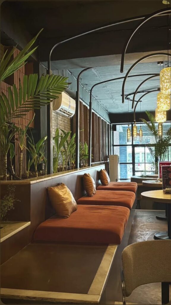 A restaurant lounge with rust-orange banquette seating, exposed brick arches, and lush greenery, designed by ZM Architects.