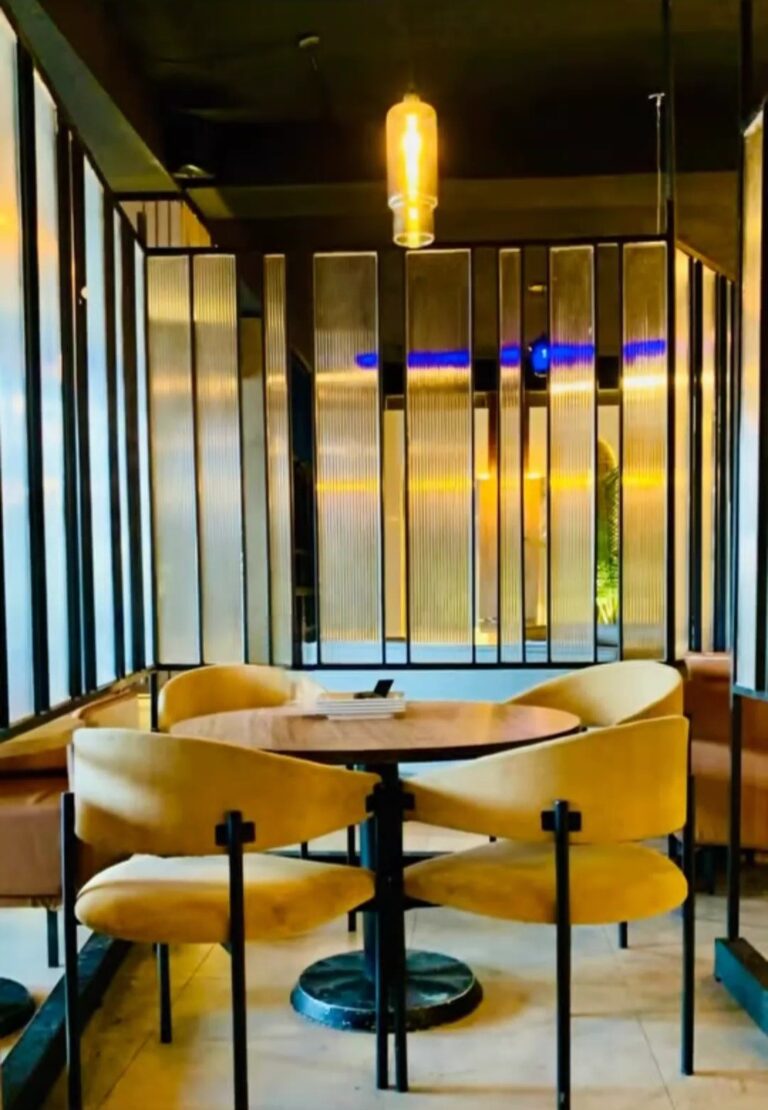 A restaurant seating nook with mustard-yellow curved booths and black mirrored panel backdrops, designed by ZM Architects.